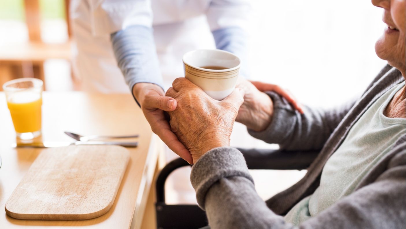 an old woman receiving a hot drink from a carer.